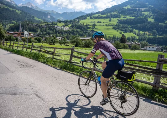 Guest cycling past mountain town, large mountain range in background.