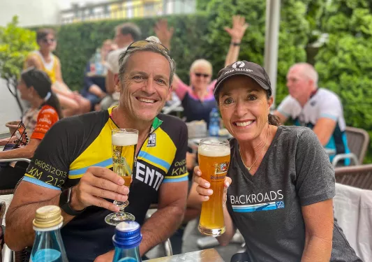 Two guests cheersing beer glasses, smiling at camera.