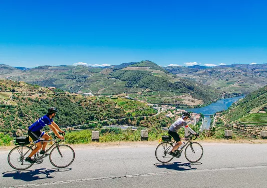 Two bikers riding on a road along the Douro River.