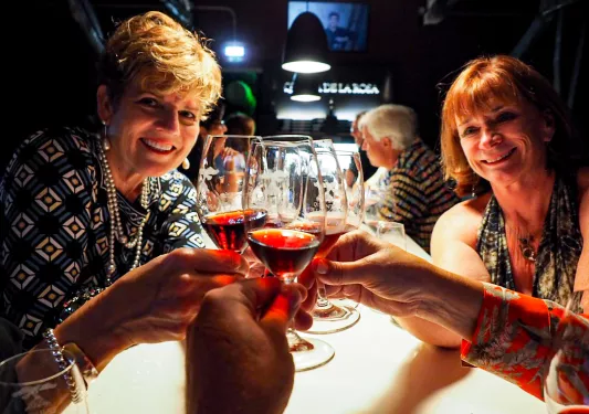 People saying cheers with glasses of red wine.