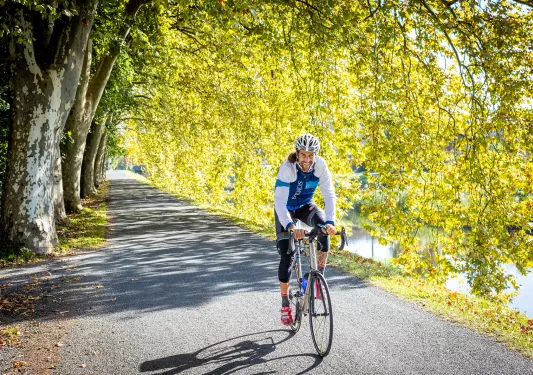 Guest/leader cycling down tree-covered road, smiling.