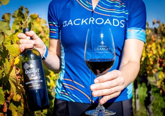 Leader in jersey with red wine bottle, glass, vineyard behind them.