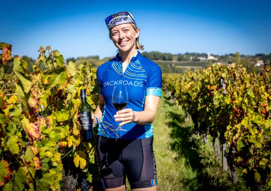Leader among grapevines, holding wine bottle, glass.