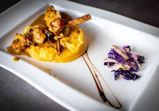 Shot of meat on mini skewers on bed of mashed potato, shredded veggies. 