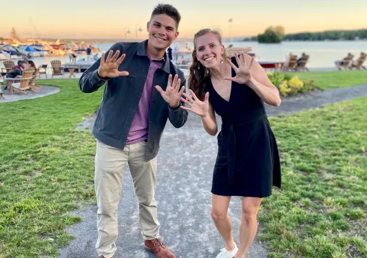 Two guests waving and posing for camera, lake and boats in bakcground.