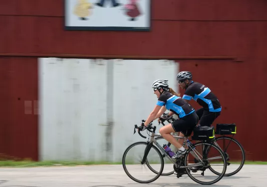 Two guests cycling past red barn.