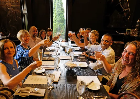 Group of guests at wooden dinner table. Toasting glasses.