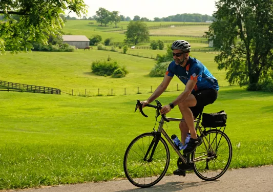 Guest cycling past farmhouses, grassy meadow.