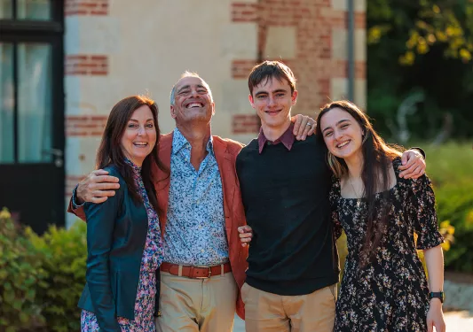 Four guests all embracing, brick building behind them.