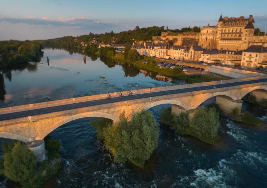 Bird's eye shot of cyclists over Loire River during sunset.  Château Royal d'Amboise behind.