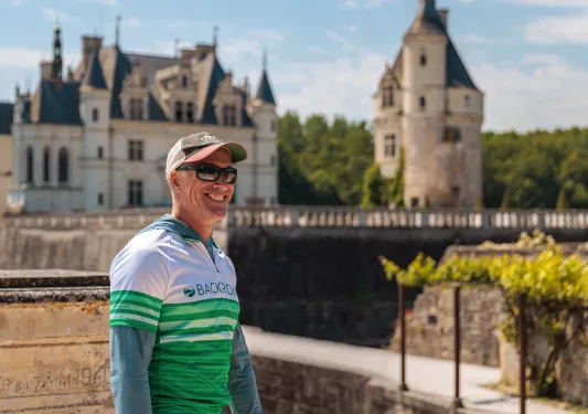 Guest smiling with green and white French chateau behind.