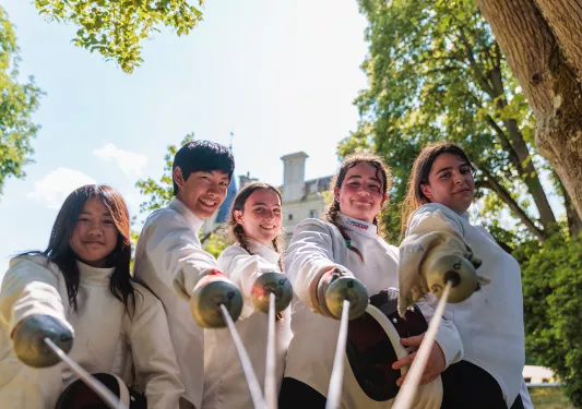 Five young guests in fencing gear, pointing sabers at camera.
