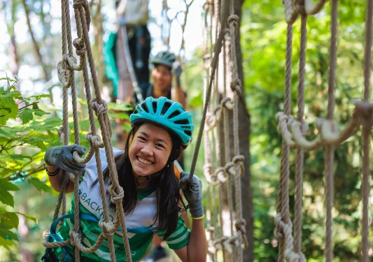 Young guest doing ropes course, smiling at camera.