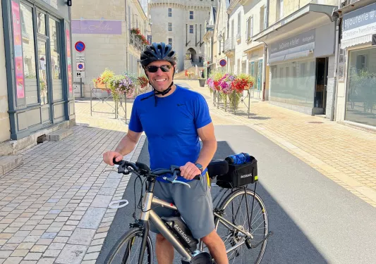 Guest with bike, standing in French road among white buildings and storefronts.
