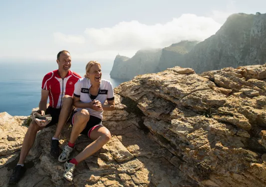Two bikers resting on rocks cliffside in Mallorca.