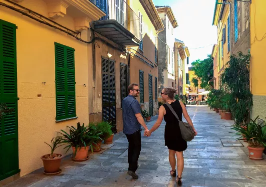 Two guests holding hands walking down an alley way in Mallorca.