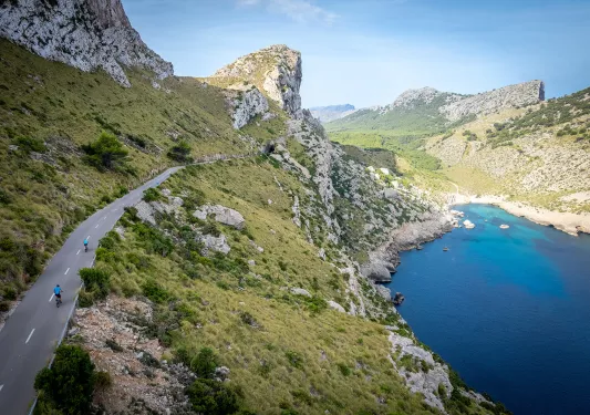 Two bikers riding around a bend on the coast of Mallorca.