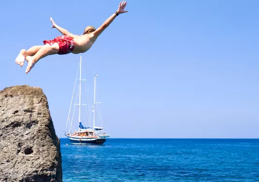 Swimmer diving off of a cliff into crystal clear waters.