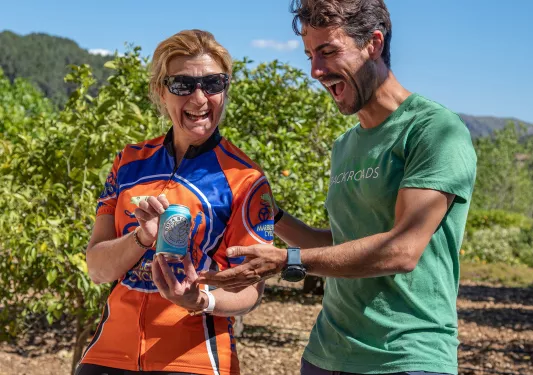 Two bikers posing with a can of wine in a vineyard.