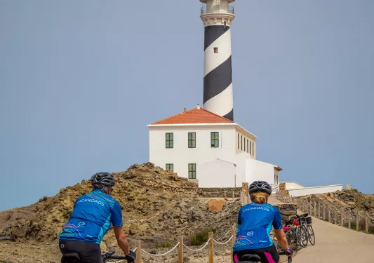 Bikers riding towards a lighthouse.