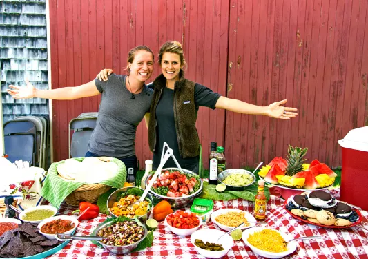 Two people posing behind lunch spread.