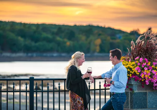 Two guests chatting, wine glasses in hand, sunset and beach in background.
