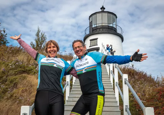 Two guests with their arms outstretched, lighthouse in background.