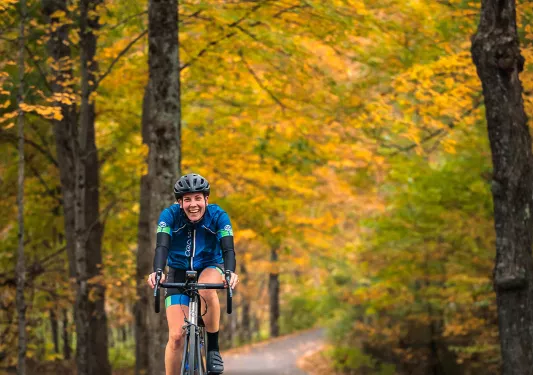Guest cycling down autumnal road, smiling at camera.