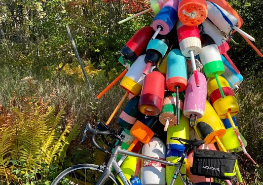 Bike parked at "LOBSTER LN" sign, numerous buoys tied around it.