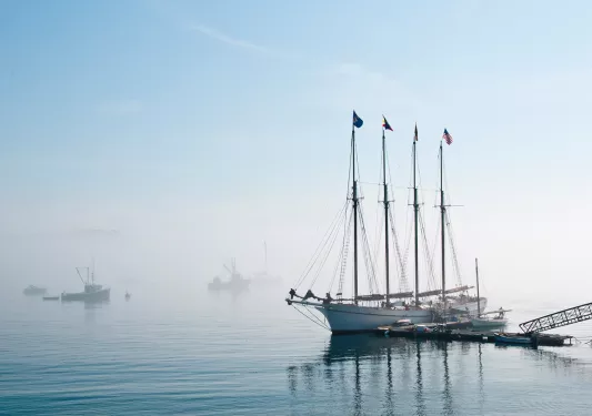 Wide shot of a four-masted ship in port, fog on the horizon.