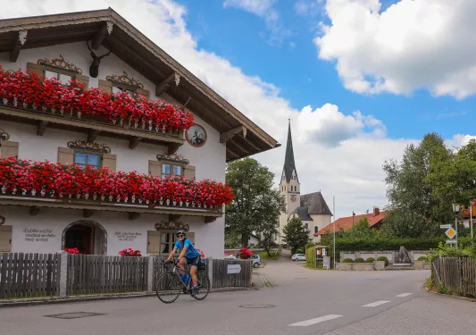Biker riding past house with large pink and red floral displays on balconies.