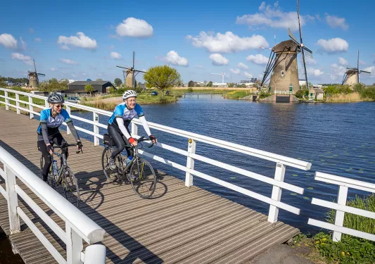 Bikers on small bridge with windmills in background