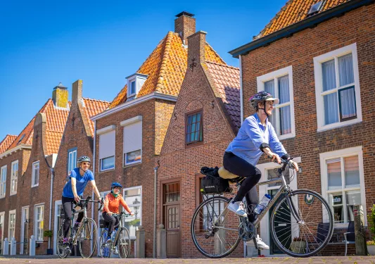 Three guests cycling past brick housefronts.
