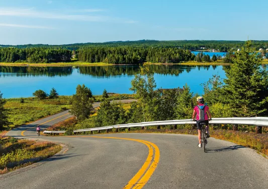Guest cycling down road, large lake or river in background.