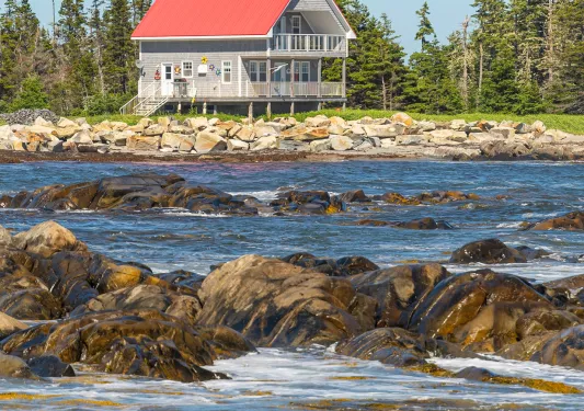 Rocky ocean shore in foreground, two-story fishing house in background.