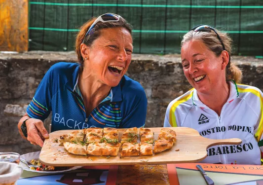 Two guests at lunch, both laughing, passing focaccia.