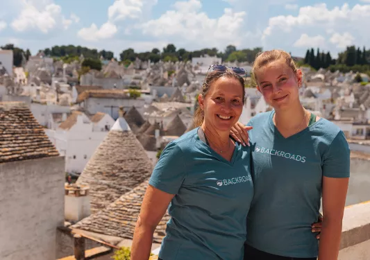 Two guests posing in front of wide shot of Alberobello.
