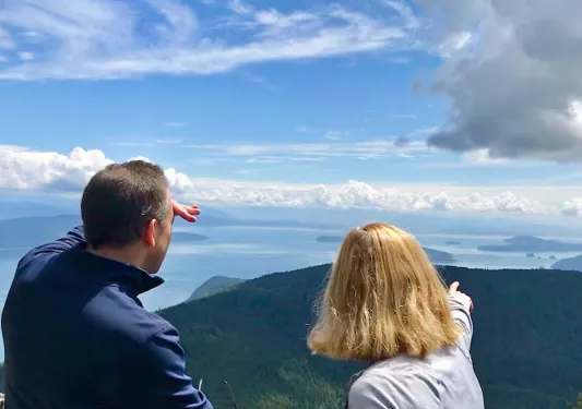 Two guests looking out over cloudy vista, forest below them.
