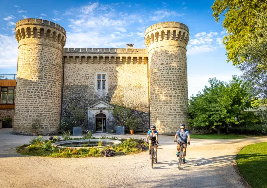 Two guests cycling in front of large stone brick castle.