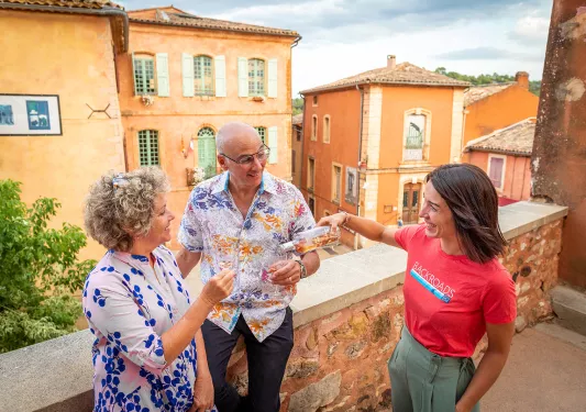 Two guests and a leader, leader pouring wine for guests, on house balcony.