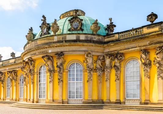 Sans Souci building in Germany, bright yellow decorated with statues of cherubs.