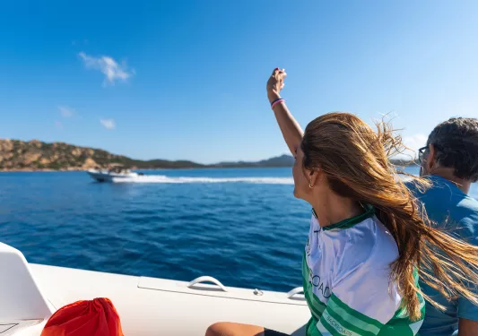 Two guests on boat, waving to another.