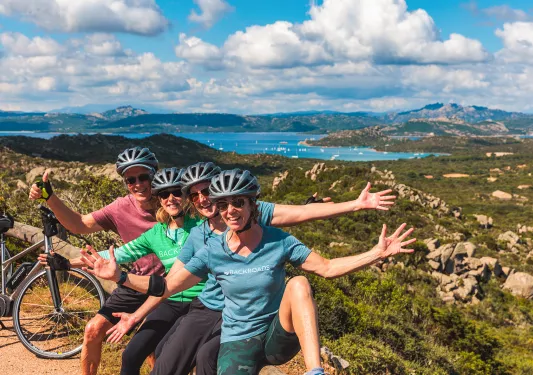 Four guests sitting on wooden fence, gesturing to vista behind them.