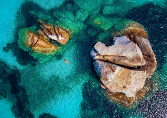 Overhead shot of guest swimming, light blue water, two large rocks.