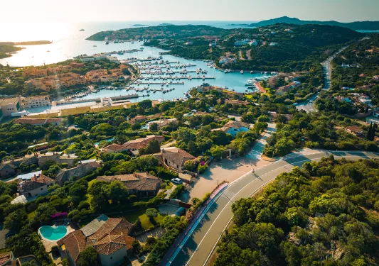 Bird's eye shot of large coastal town, houses, pools, piers in distance. 