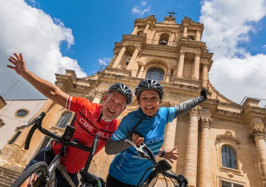 Two bikers posing in front of church with their bikes.