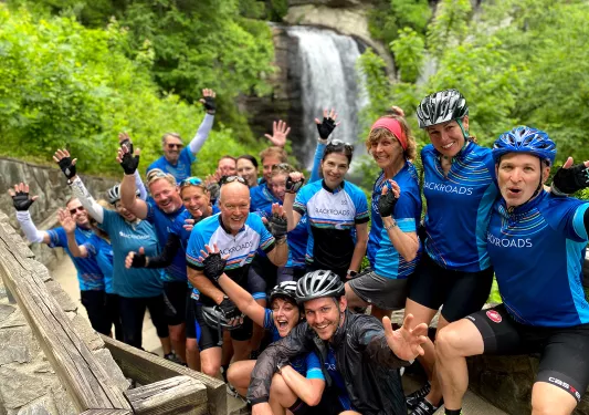 Group of guests in biking gear, waterfall behind them.