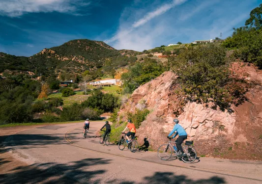 Four guests rounding a corner, hilltop houses and Cali hills in background.