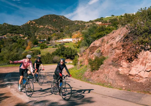 Three guests rounding corner, one pointing towards camera, Cali hills in background.