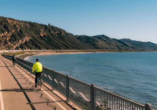 People biking along coastal road, ocean beside them.